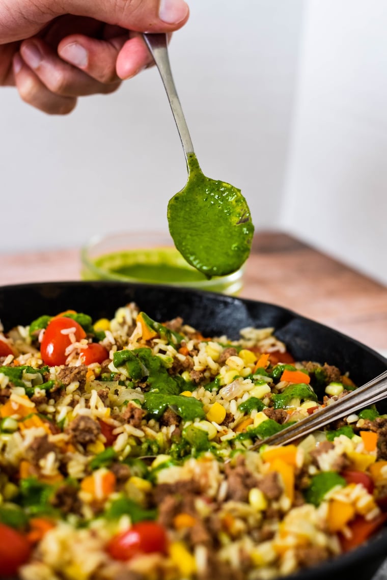 drizzling chimichurri sauce on ground beef and rice in skillet