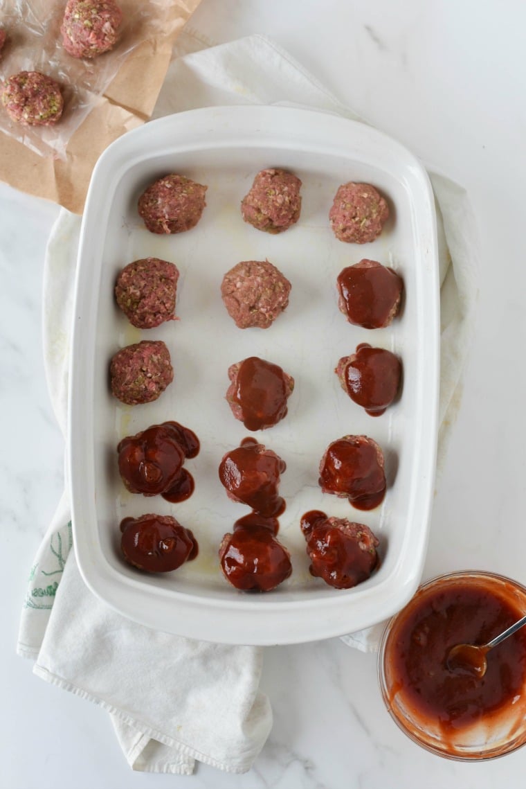 baking dish with beef meatballs and glaze being added