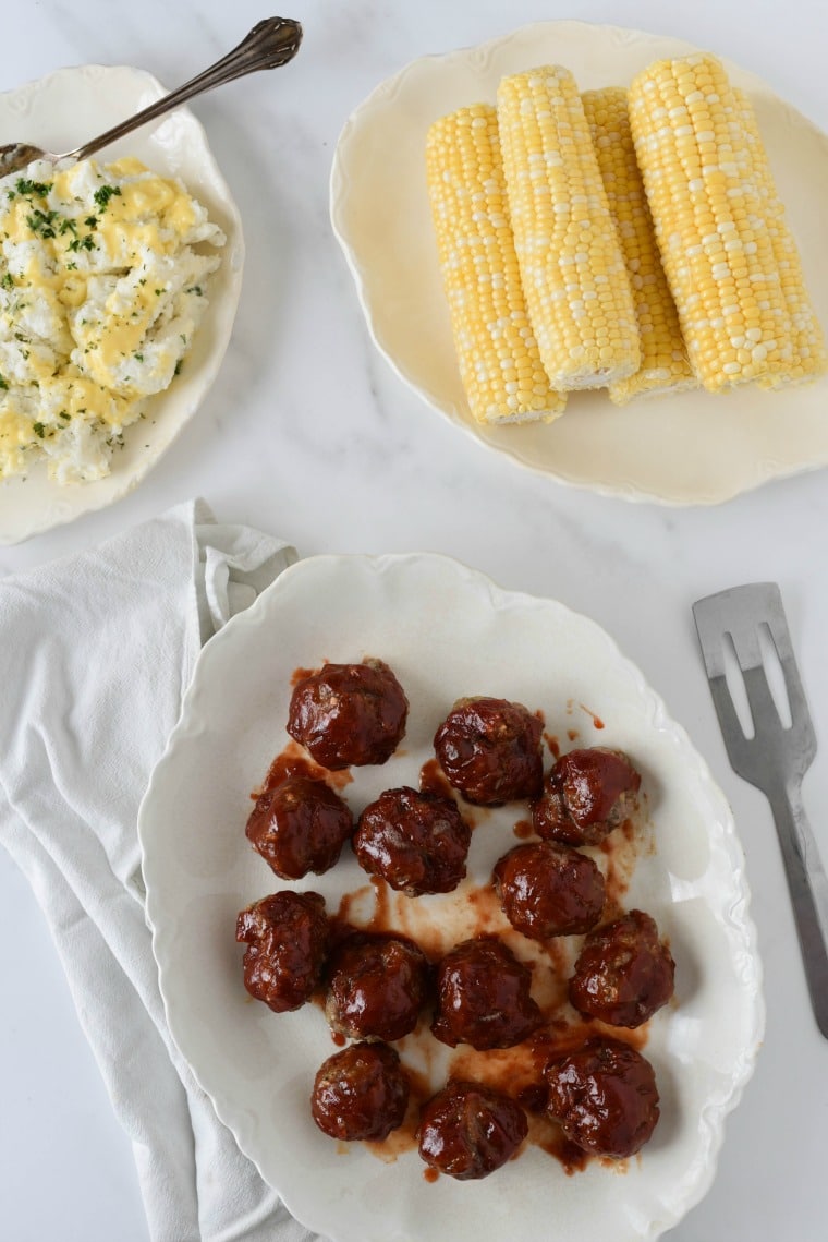 platter of meatballs with meatloaf glaze next to mashed potatoes and corn