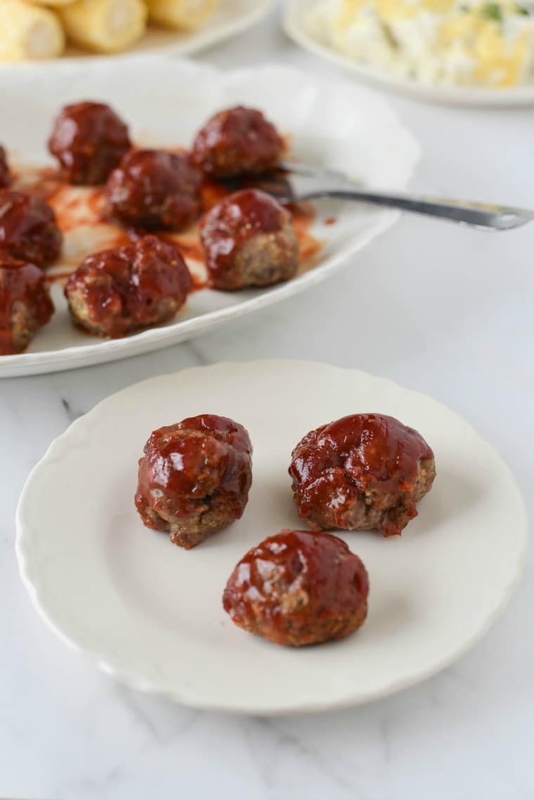 white plate with three meatloaf meatballs next to platter 