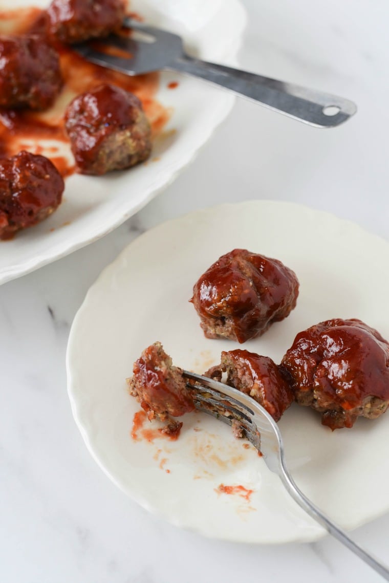 A plate of meatballs with glaze with a fork and knife