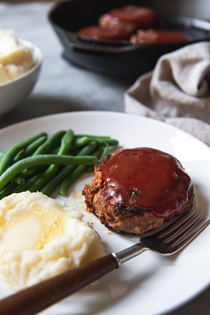 a plate with meatloaf, mashed potatoes and green beans