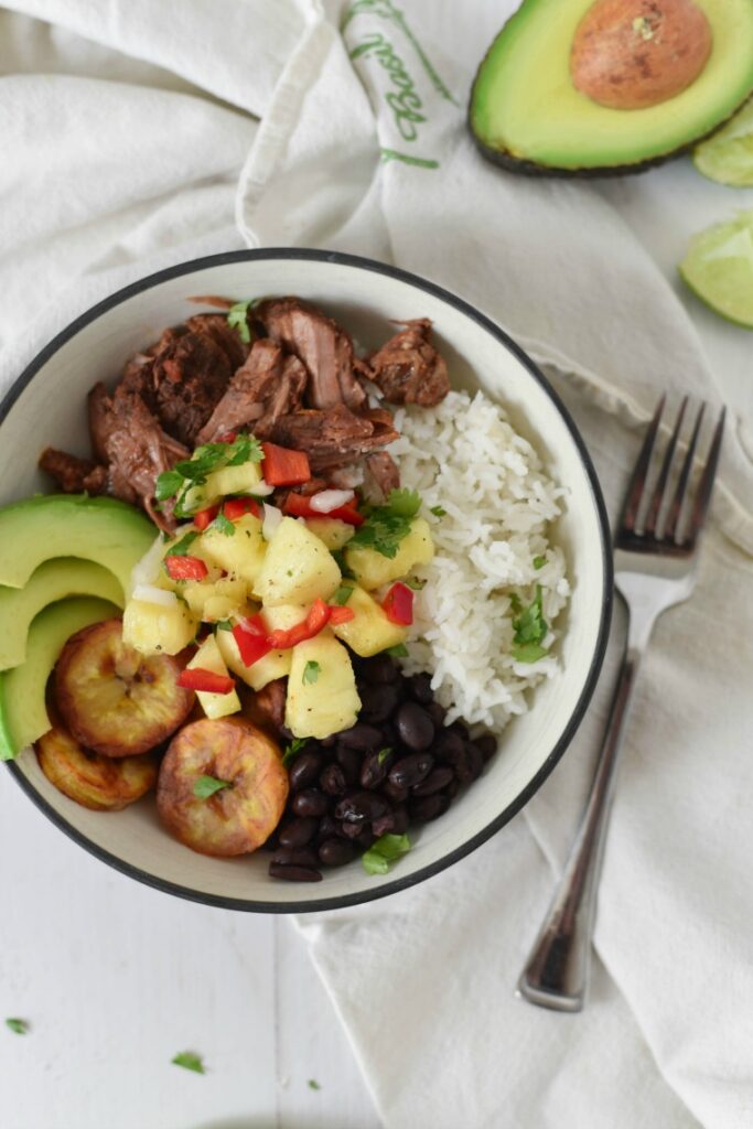 bowl with cuban beef, rice, beans, plantains, avocado slices and pineapple salsa