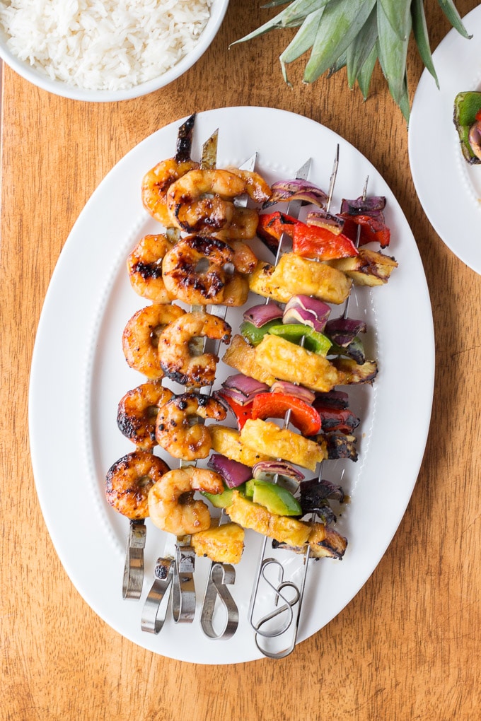 white platter with skewers of grilled shrimp and vegetables and pineapple