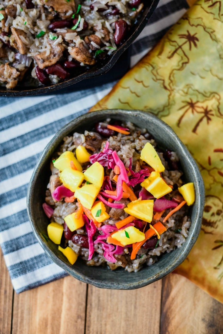 A bowl of food on a wooden table, with Jerk chicken and pineapple Salsa