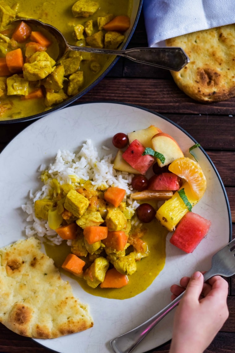 A plate of food on a table, with Chicken curry, rice and fresh fruit