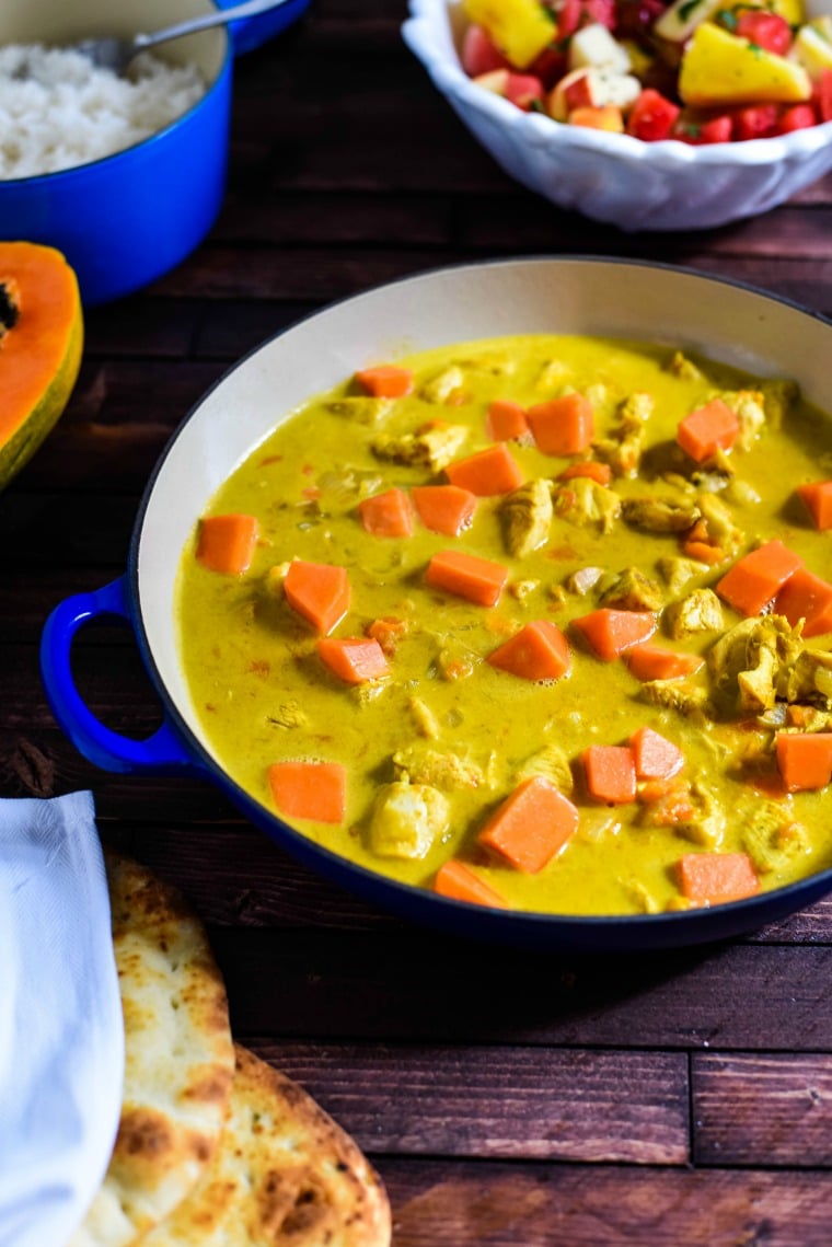 a serving bowl of chicken curry with papaya on wooden table