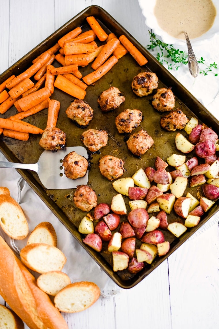 a sheet pan with roosted carrots, meatballs and potatoes with serving utensil
