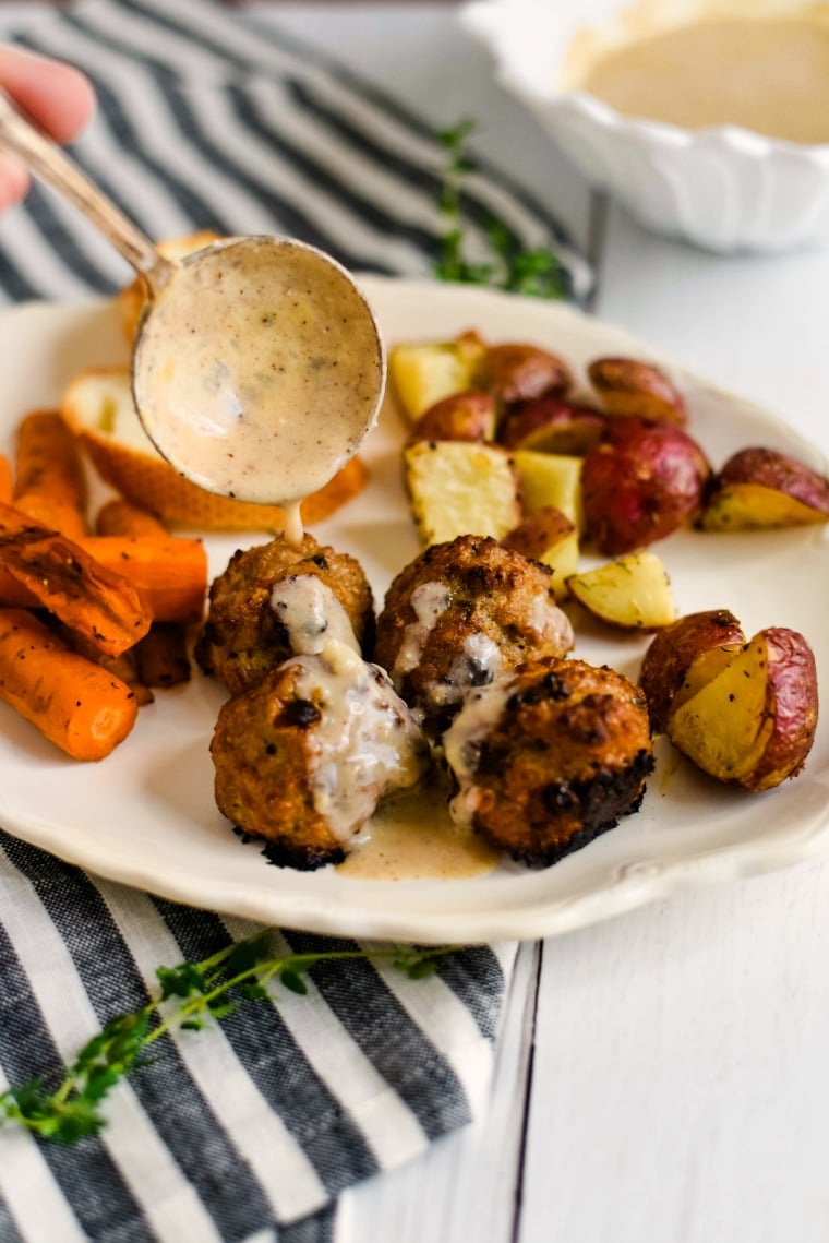 A plate of food, with pork Meatball, roasted carrots, and roasted potatoes with gravy being drizzled on