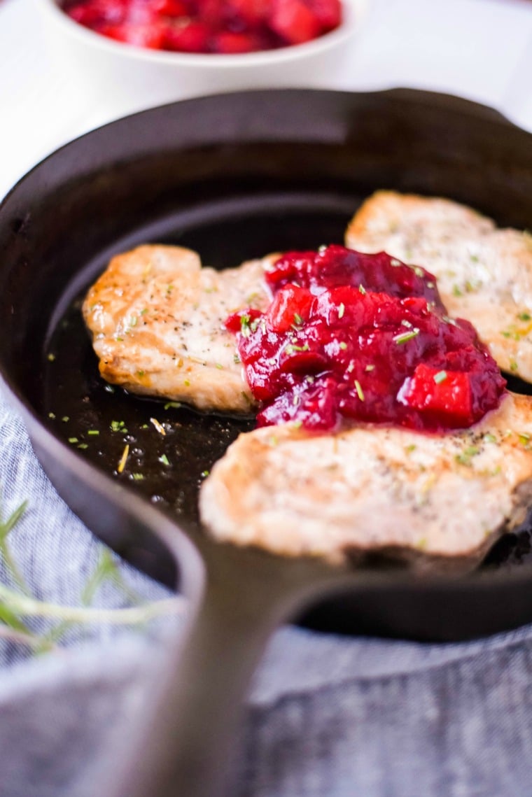 rosemary pork chops in cast iron skillet topped with cranberry sauce