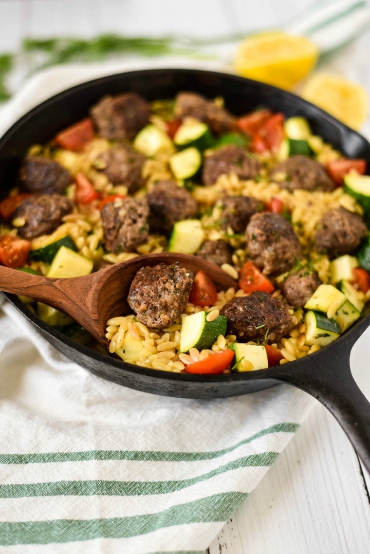 Cast iron skillet with greek meatballs and orzo being scooped with wooden ladle