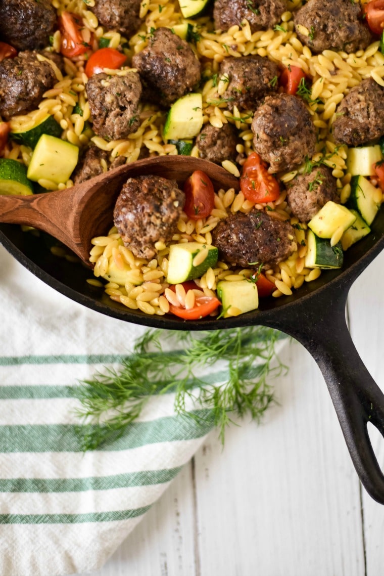 Greek meatballs in cast iron skillet with orzo, tomatoes and zucchini