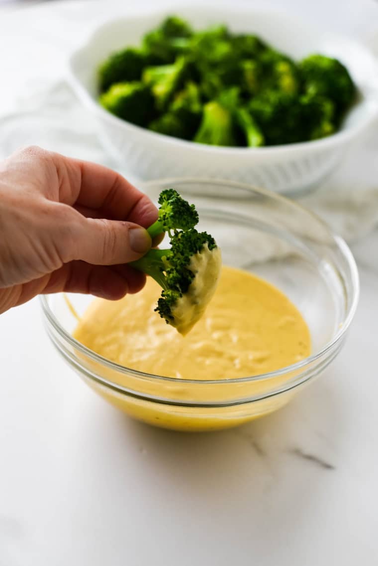 a hand holding broccoli and dipping it into cheese sauce