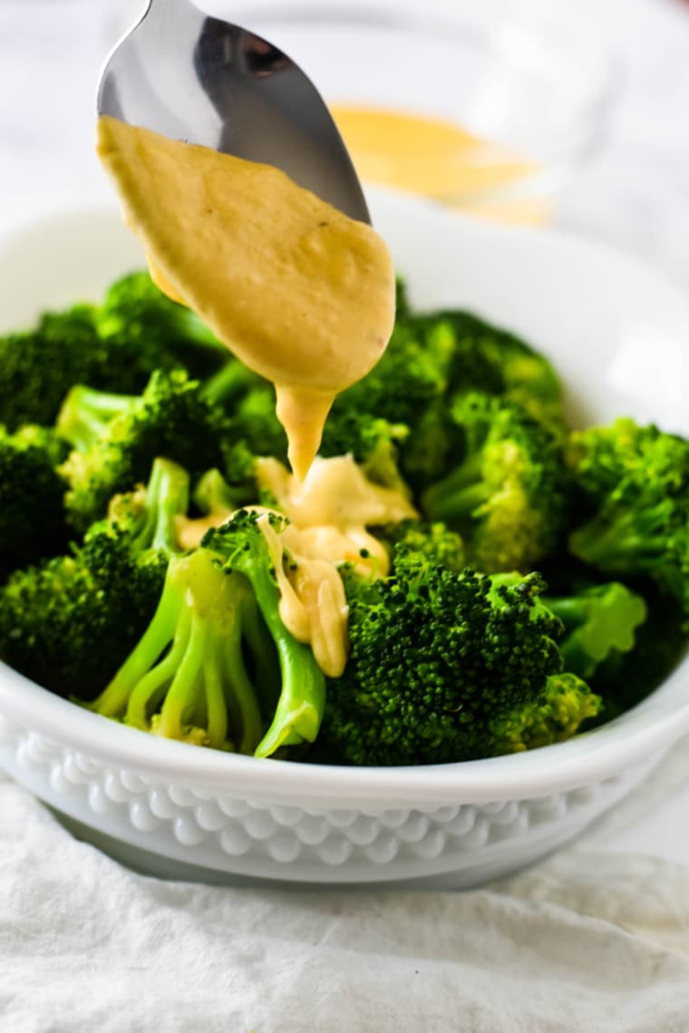 cheese sauce being dribbled on broccoli