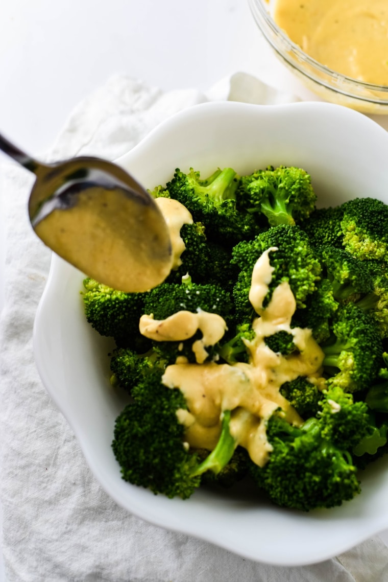 a spoon putting cheese sauce on broccoli