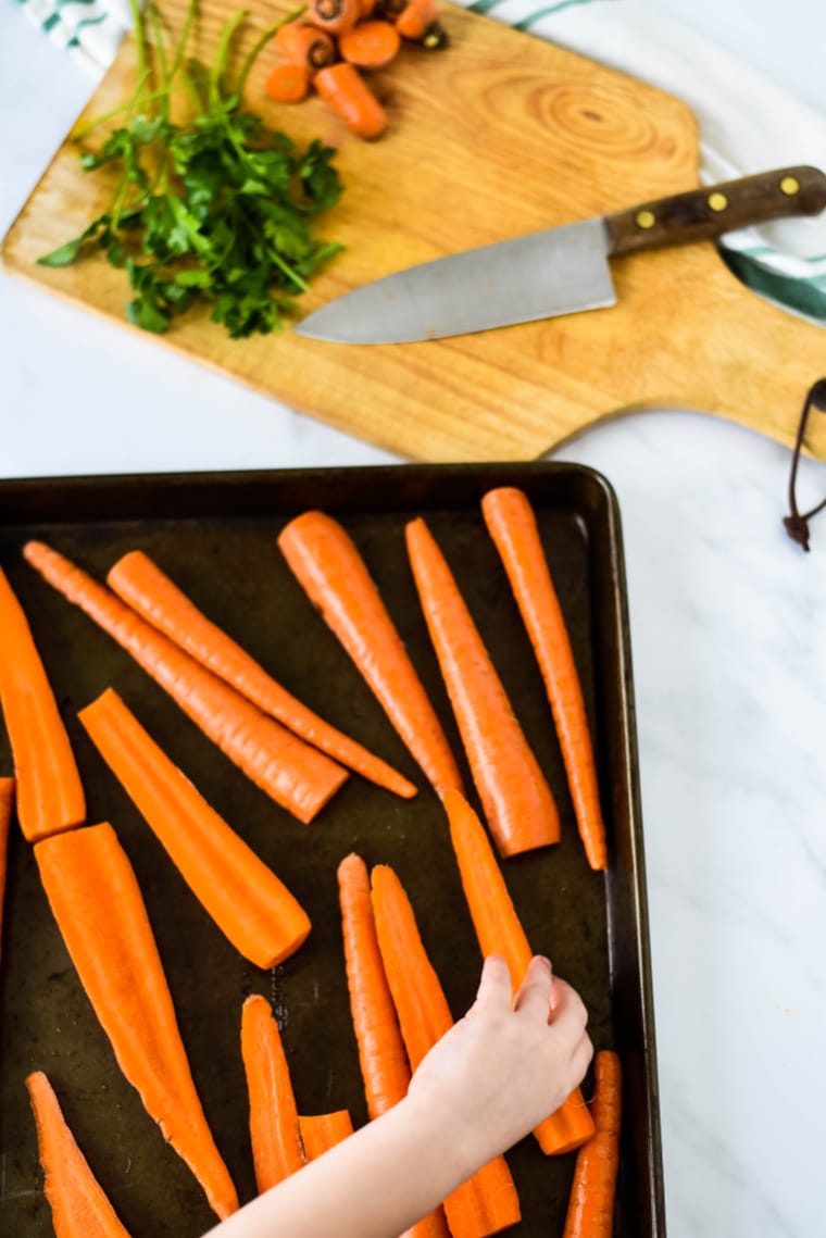 childs hand arranging carrots on baking sheet