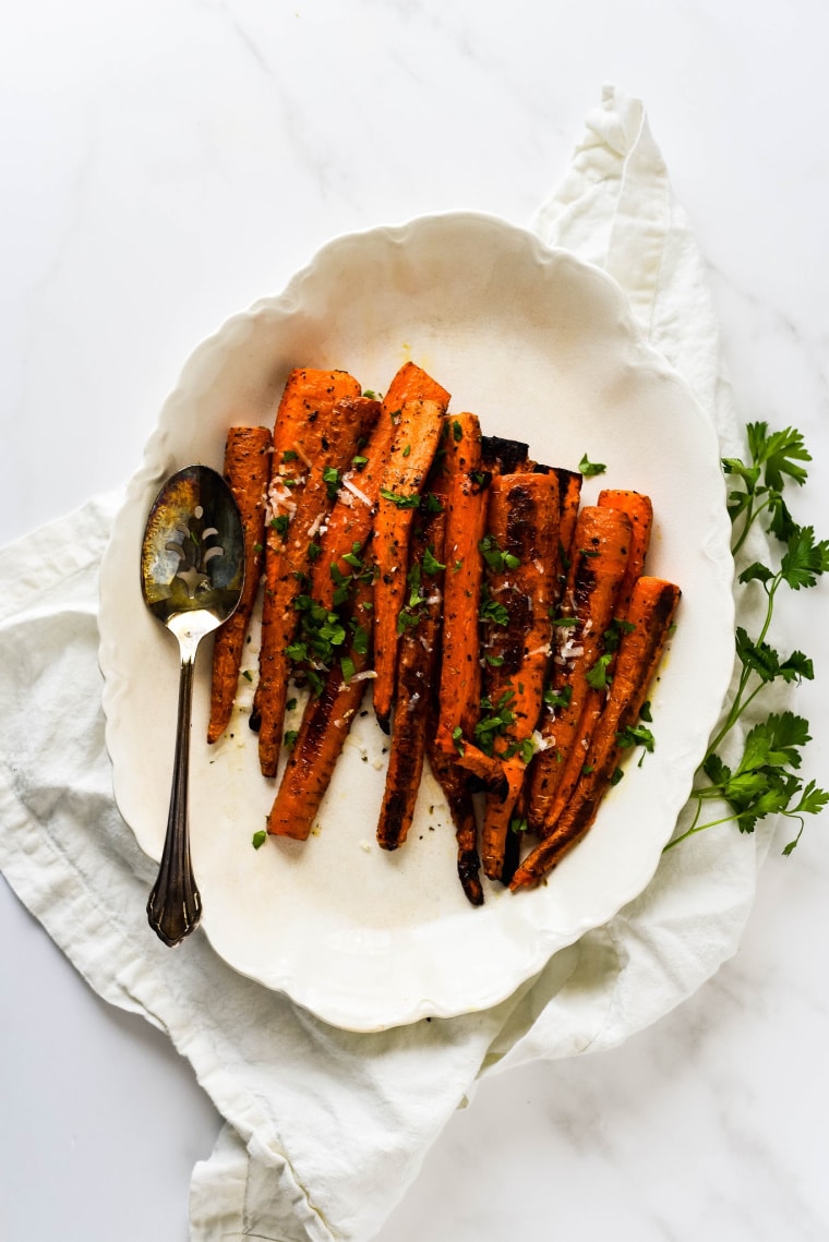 overhead image of herb carrots on white platter with serving spoon