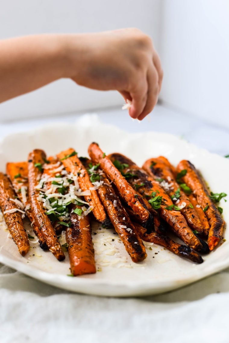 hand sprinkling grated parmesan on roasted carrot recipe