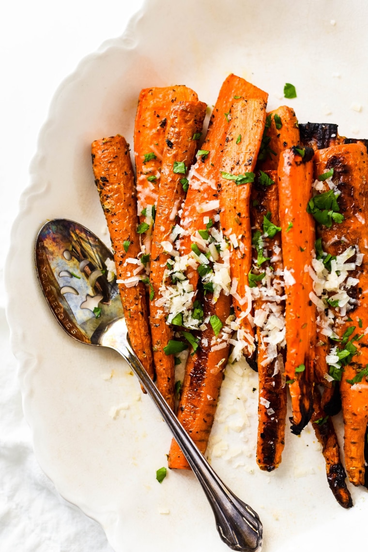 close up of italian herb roasted carrots on white platter with spoon