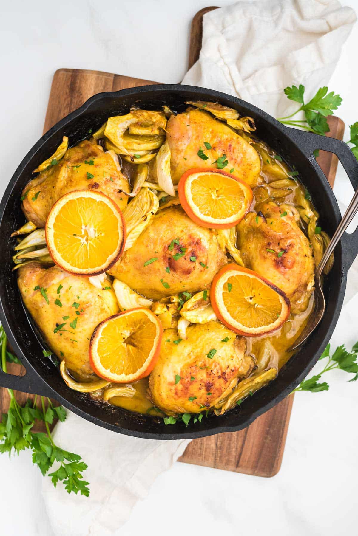 overhead view of cast iron skillet with chicken thighs and orange slices