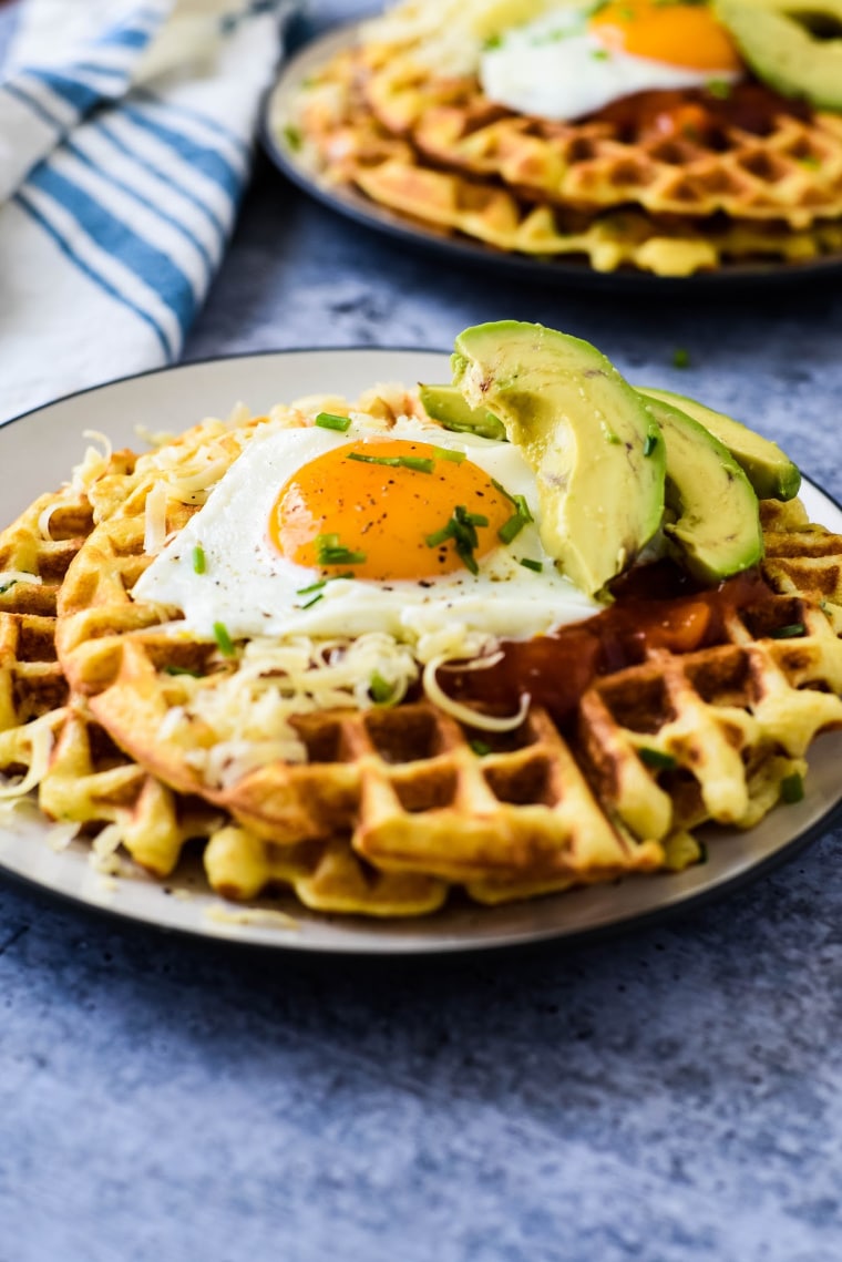 cornmeal waffles on a plate with eggs and avocado slices