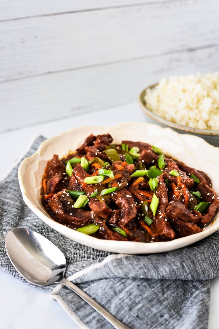 Bowl of Slow Cooker Mongolian Beef with rice in background