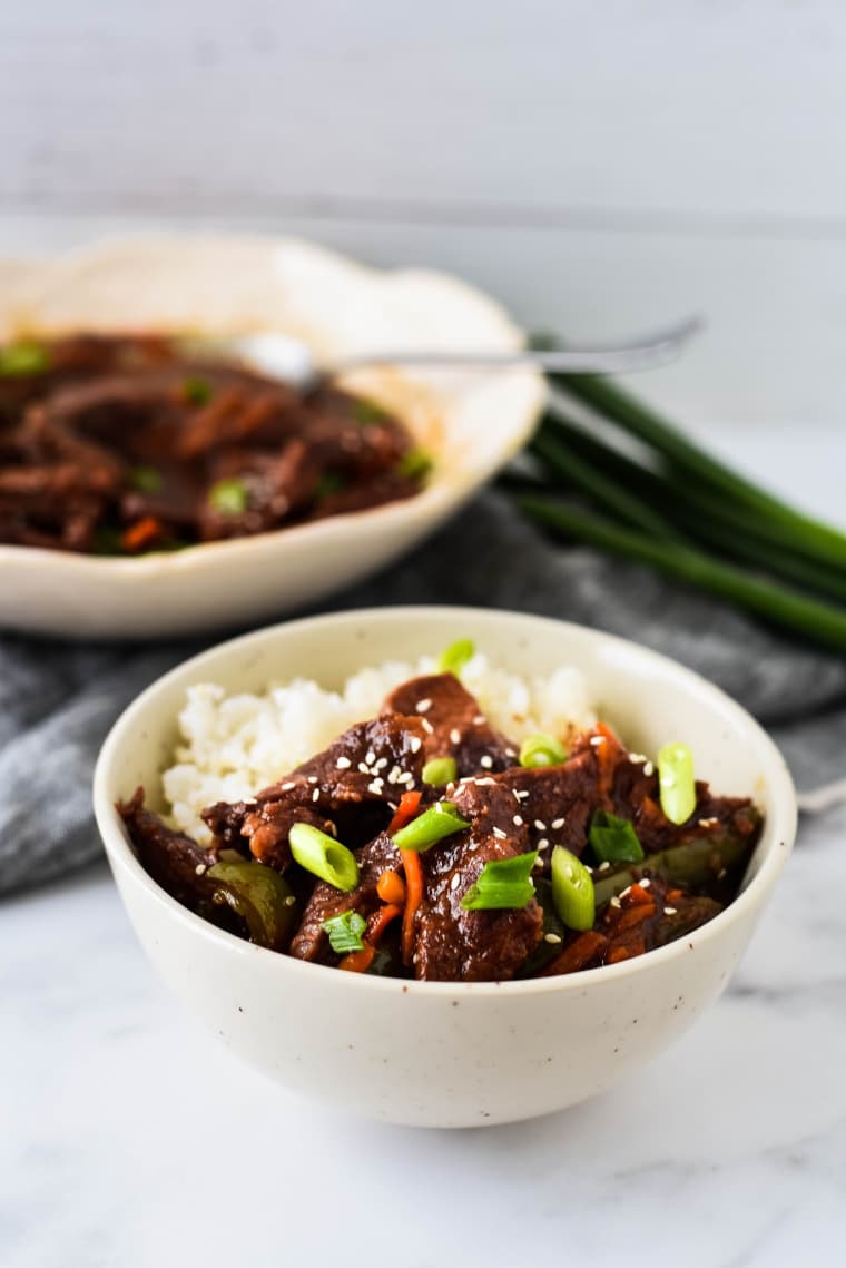 bowl with mongolian beef and rice with serving bowl in background