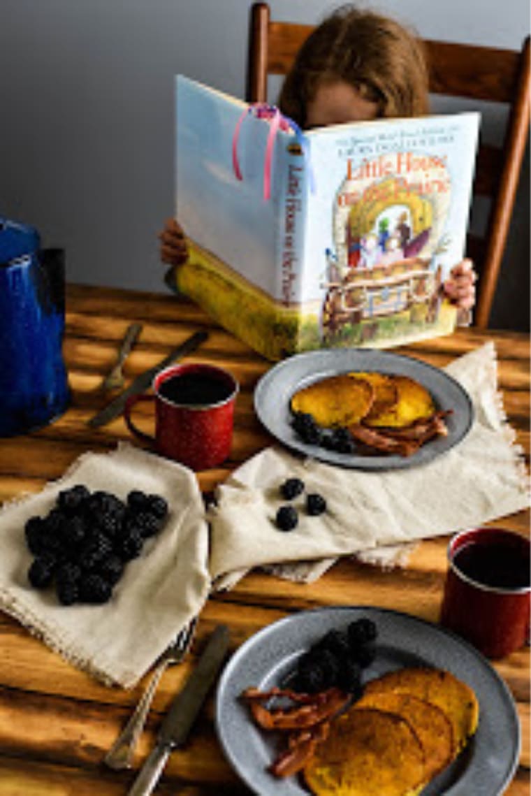 girl reading little house on the prairie with corn cakes 