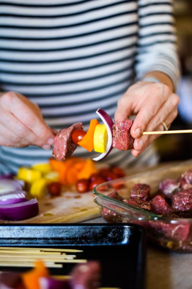 adding ingredients to skewers of za'atar beef kabobs