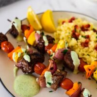 two skewers with za'atar beef and vegetables next to couscous on plate