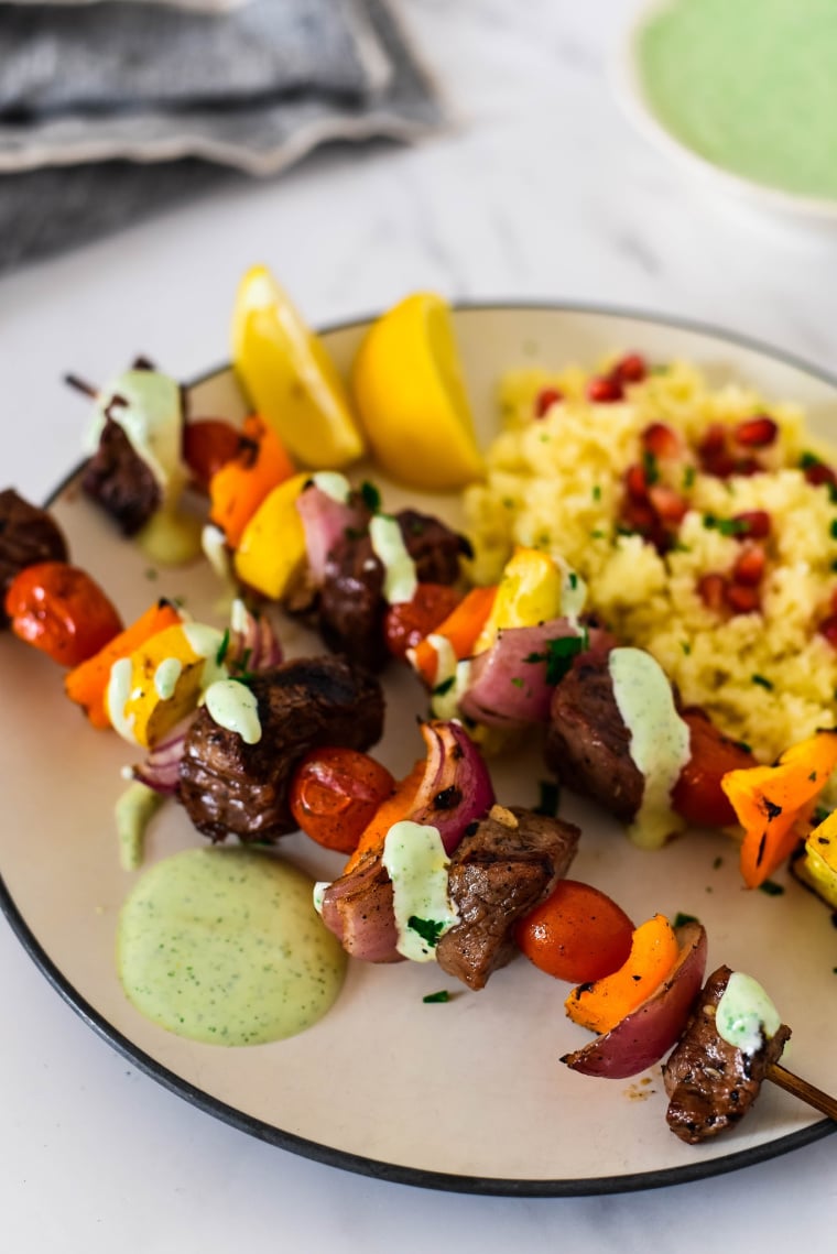 two skewers with za'atar beef and vegetables next to couscous on plate