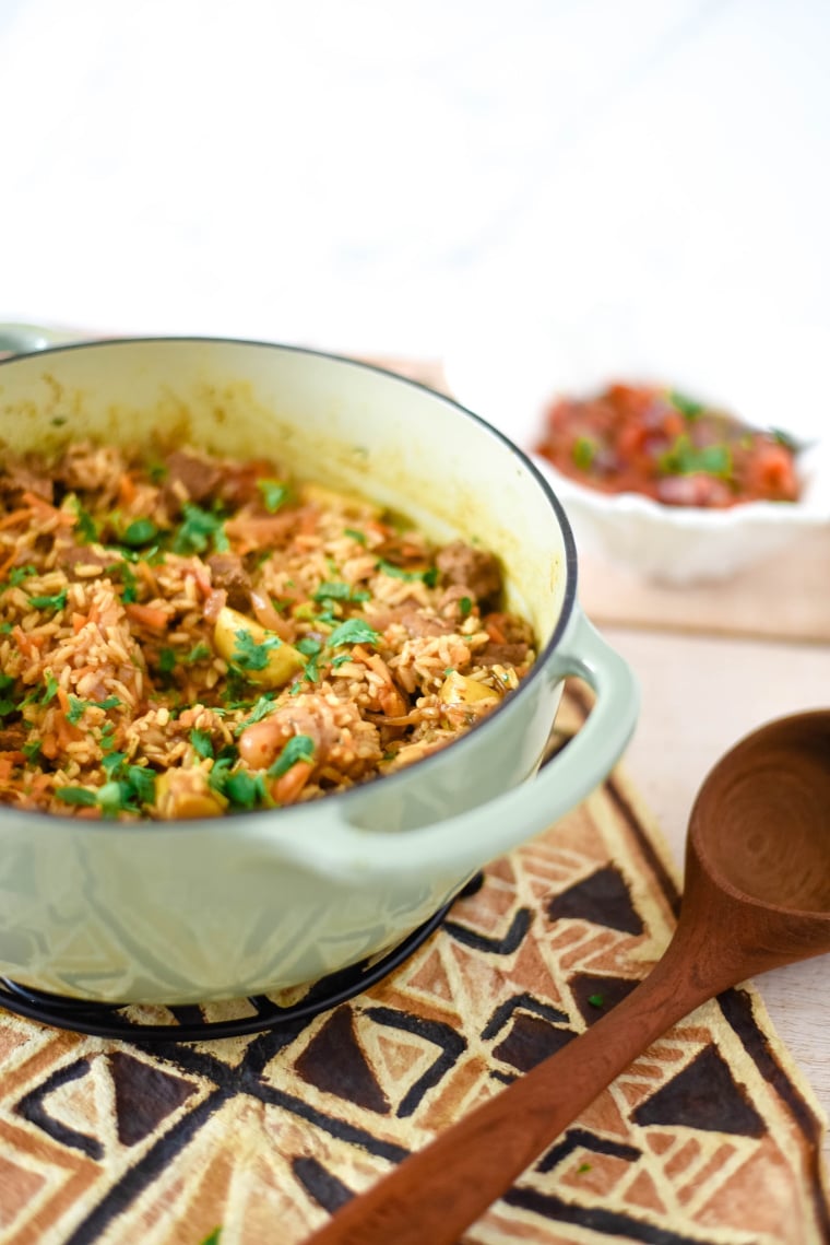 enameled cast iron pan with beef pilau, wooden serving spoon beside