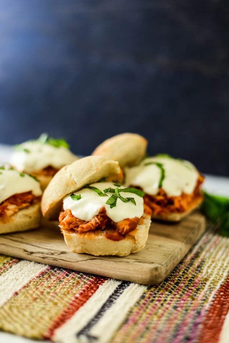 chicken sandwiches on wooden board, topped with melted mozzarella cheese and sliced basil
