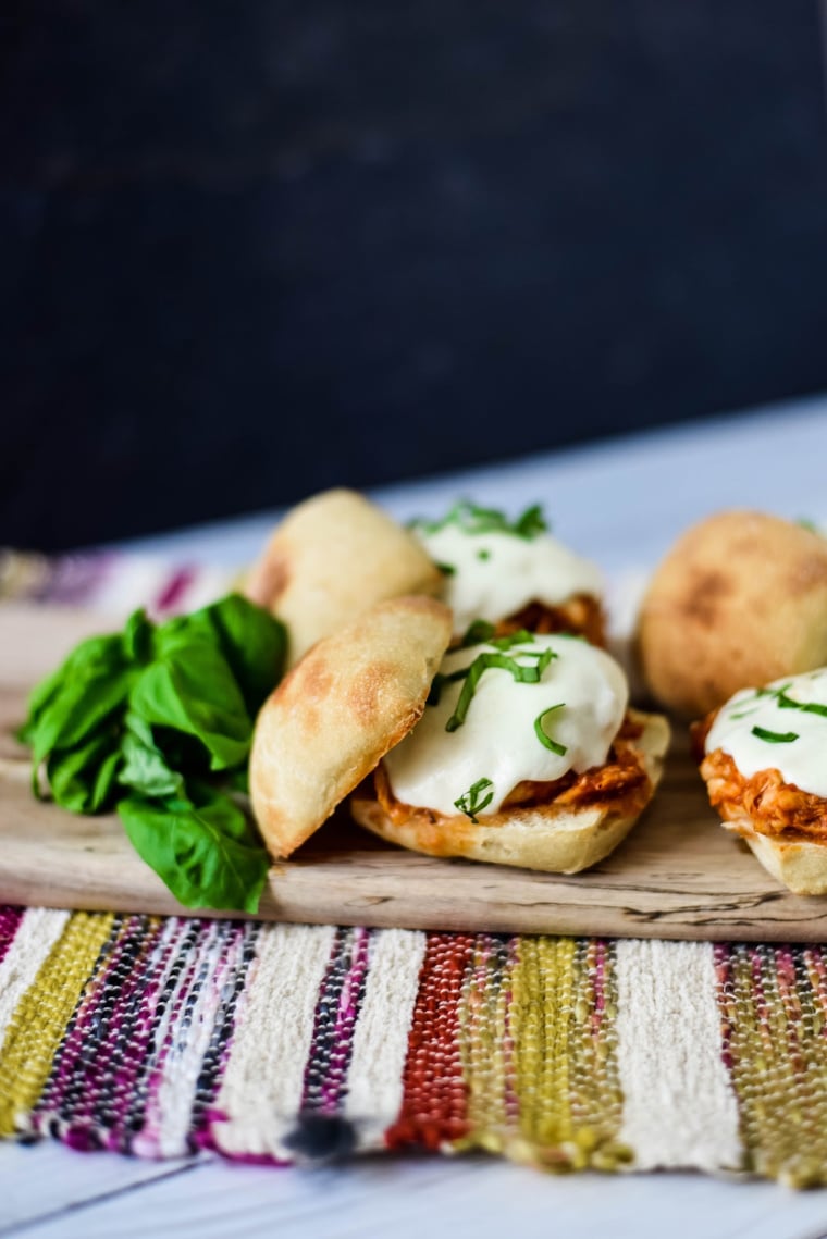 chicken parmesan sandwiches on wooden board with fresh basil beside