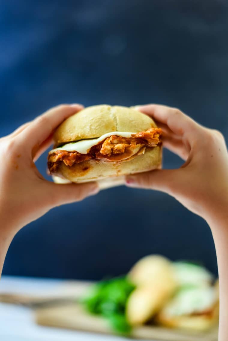 child's hands holding chicken sandwich with melty cheese