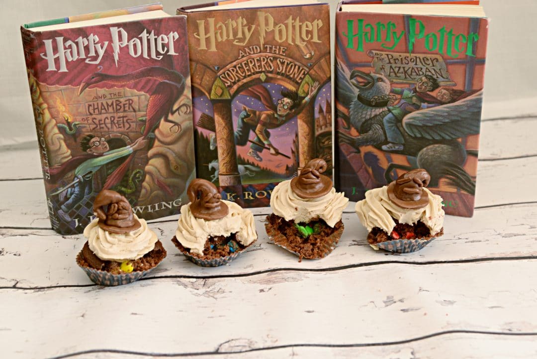 cupcakes that have colored candies inside and sorting hat chocolates on top of frosting, in front of harry potter books