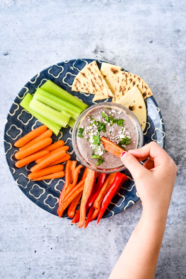 kid eating black bean dip with colorful vegetables