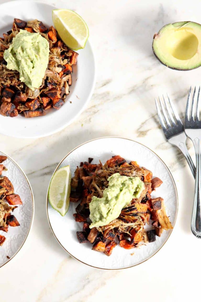 two plates with carnitas with sweet potatoes topped by avocado crema