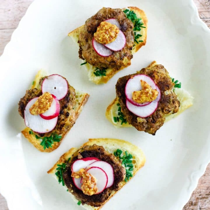german meatball on bread with radishes and mustard on white platter
