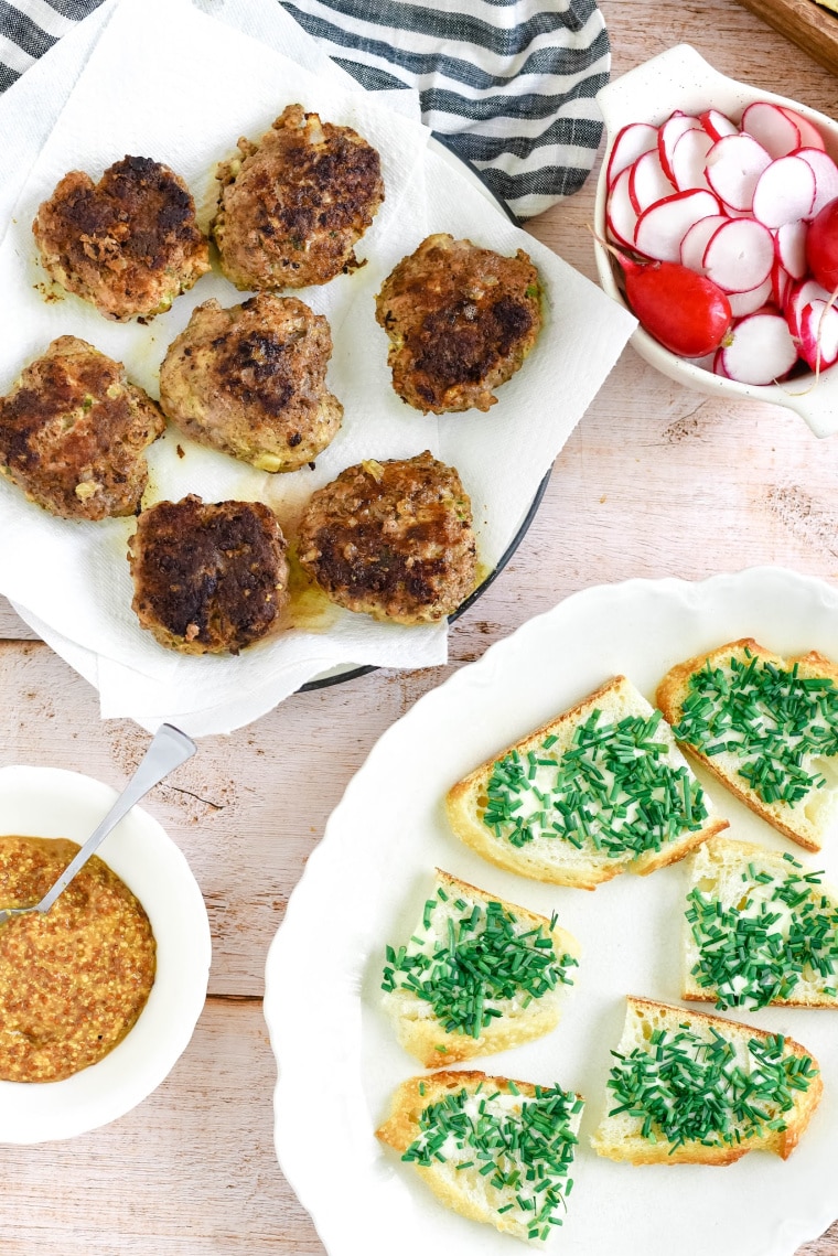 platters of german meatballs, radishes, mustard, and bread with chives on table