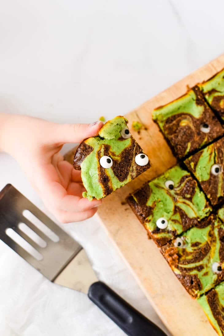 child hand taking halloween brownie off of serving board