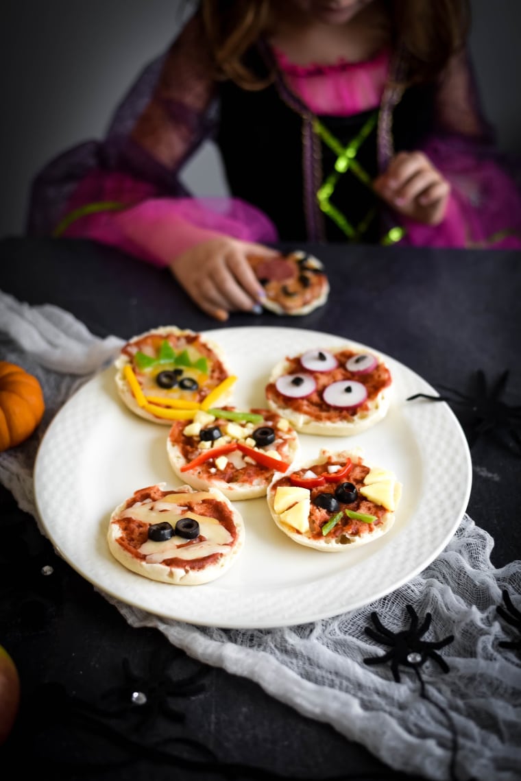  little girl dressed as witch with plate of halloween pizzas