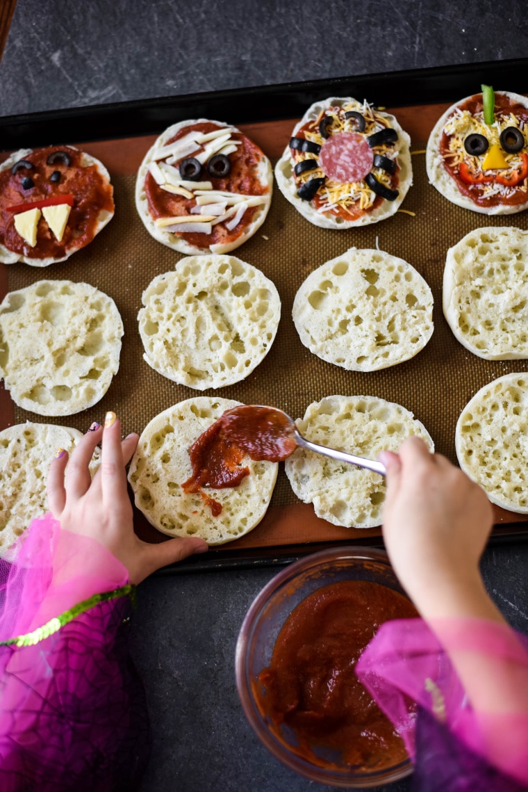 little girl spooning marinara sauce on english muffins