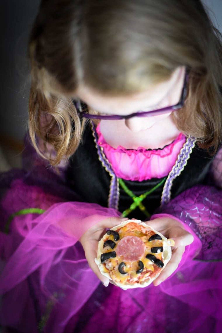 girl dressed as witch holding halloween pizza