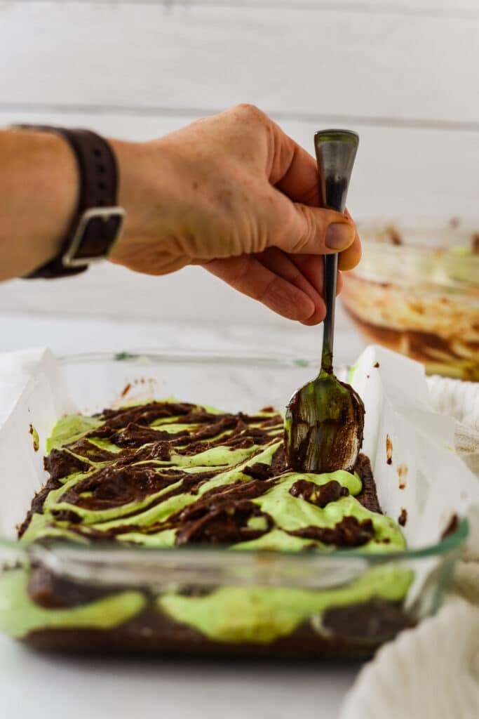 hand holding spoon and creating swirl patterns in matcha cheesecake brownies