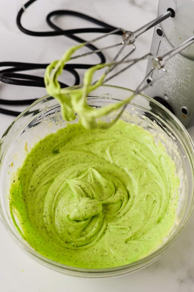 matcha cheesecake batter mixed in glass bowl with hand mixer beside bowl