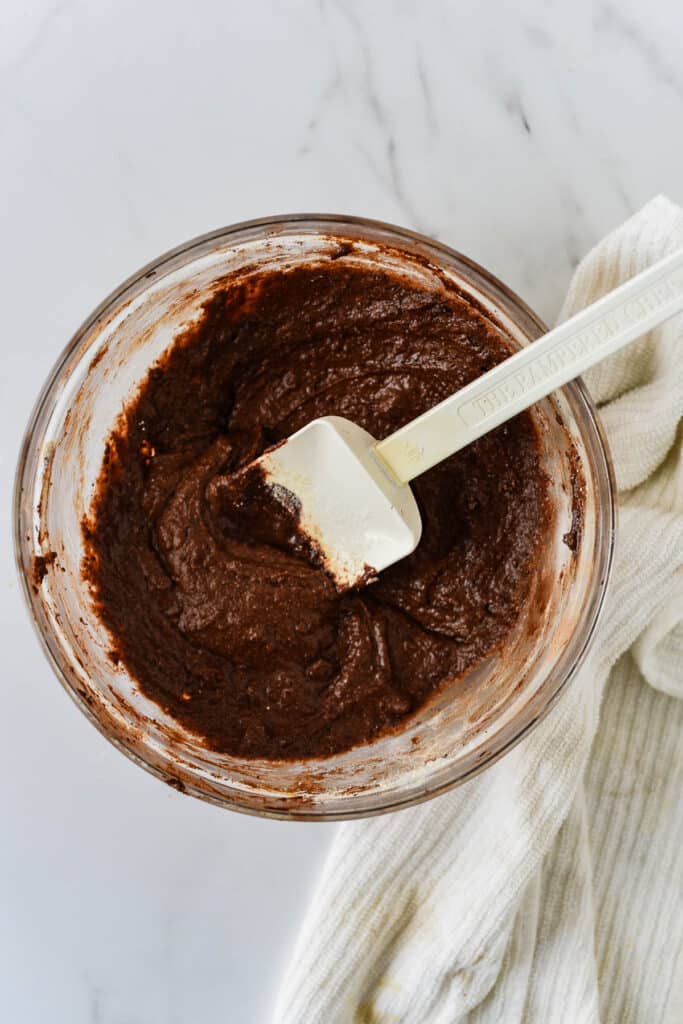 glass mixing bowl with brownie batter and white rubber spatula