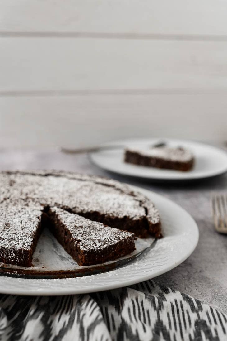 chocolate sticky cake with two pieces removed on white platter