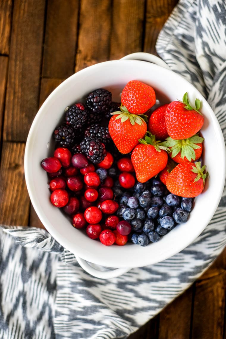 mixed berries in white bowl on wood background