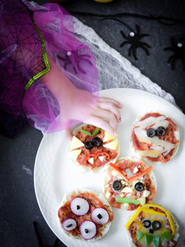 girl taking halloween pizza off of white plate